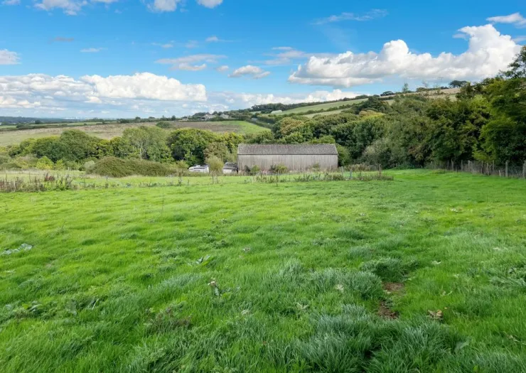 Lush green field with a barn, trees, and rolling hills under a blue sky.