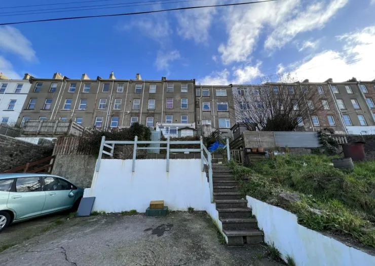 Backyard of terraced houses with steps leading up a sloped garden, fenced yard, and a parked car.