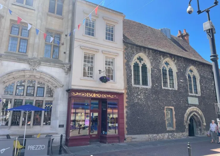 Boho" storefront between Prezzo and flint-walled historic building with arched windows.