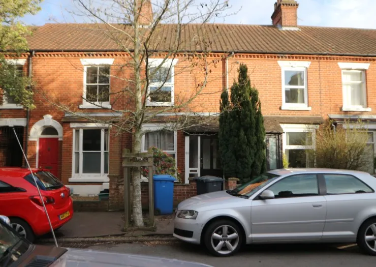 Red brick terraced house exterior with red front door, white trim, and parked cars.