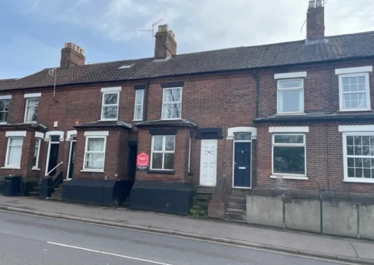 Row of brick terraced houses with "For Sale" sign, seen from street level.