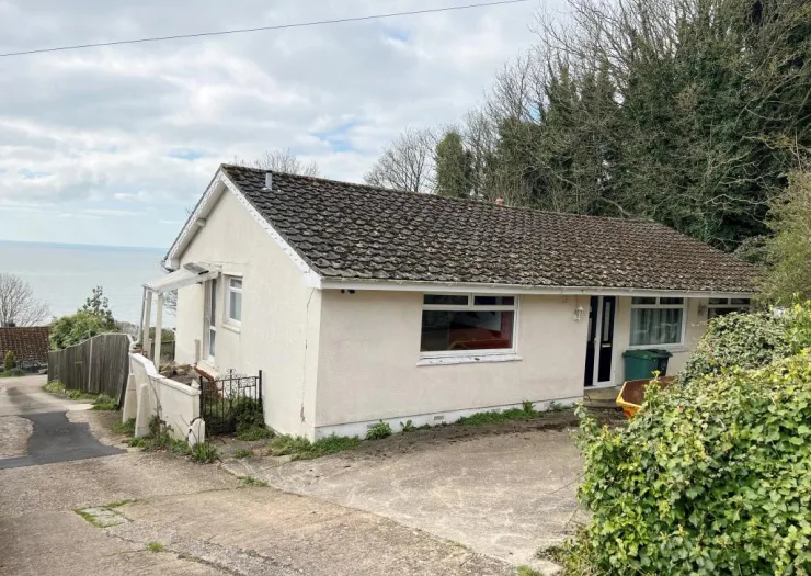 White bungalow with tiled roof, small porch, and ocean view.