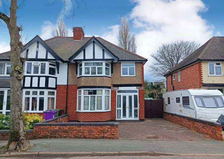 Red brick house with mock Tudor features, white windows, and paved driveway.