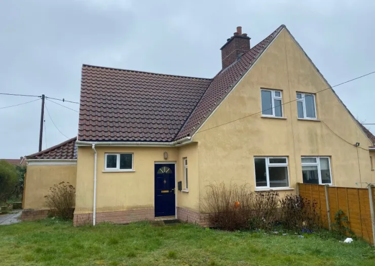 Yellow detached house with brown tiled roof, blue front door, and front garden.