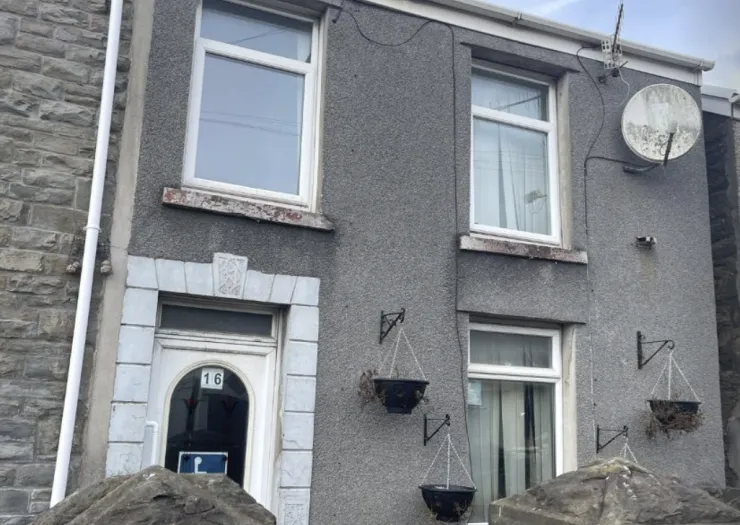 Gray terraced house exterior with white trim, hanging planters, and visible house number 16.
