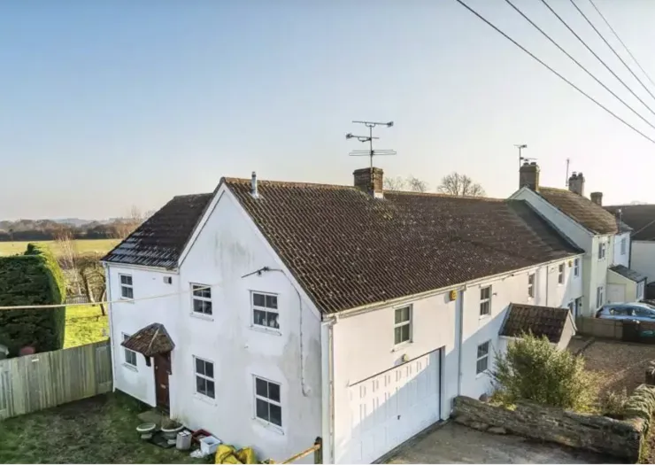 White detached house with tiled roof, attached garage, and green yard. Rural setting.