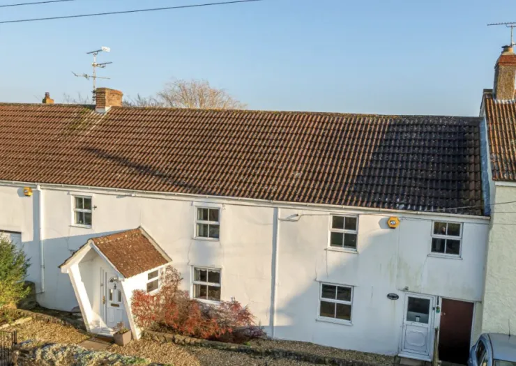 White detached house with brown tiled roof and quirky angled porch.