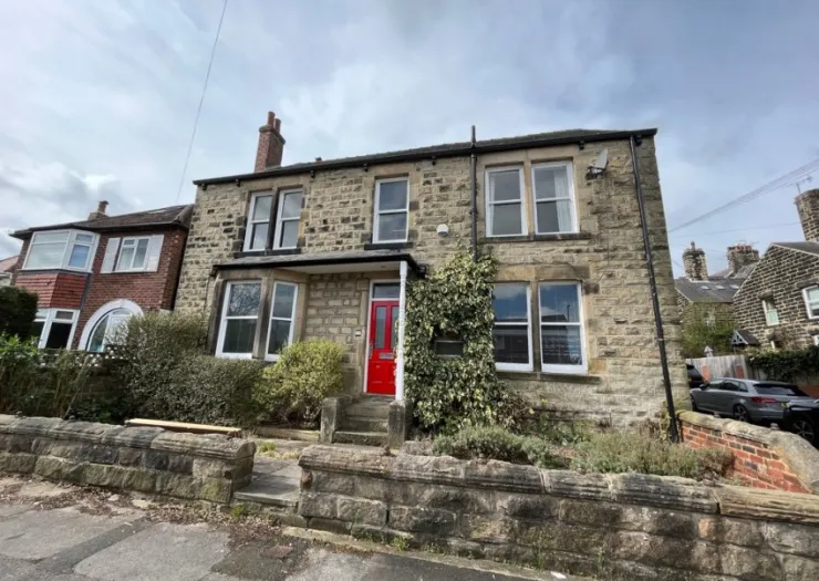 Stone house with red door, white-framed windows, and a low stone wall.