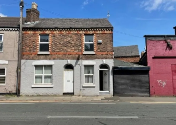 Brick terraced house with partially painted facade, open front door, and attached garage.