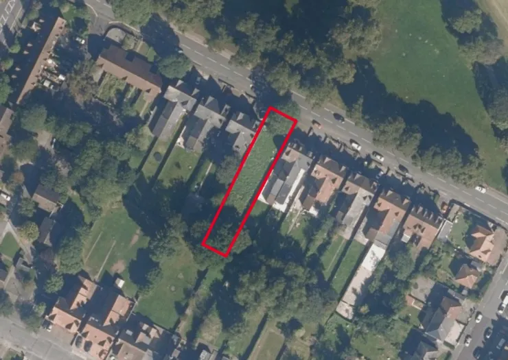 Aerial view of a vacant lot outlined in red, situated between residential properties and a road.