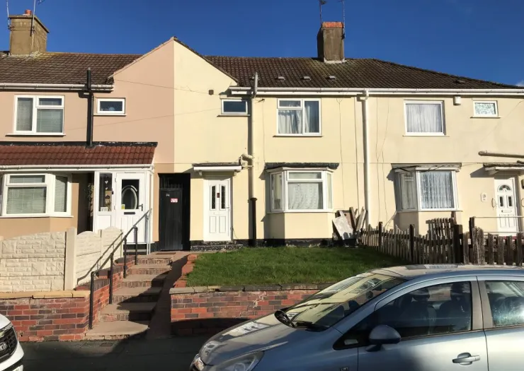 Attached terraced houses with contrasting beige and cream exteriors, front gardens, and a parked car.
