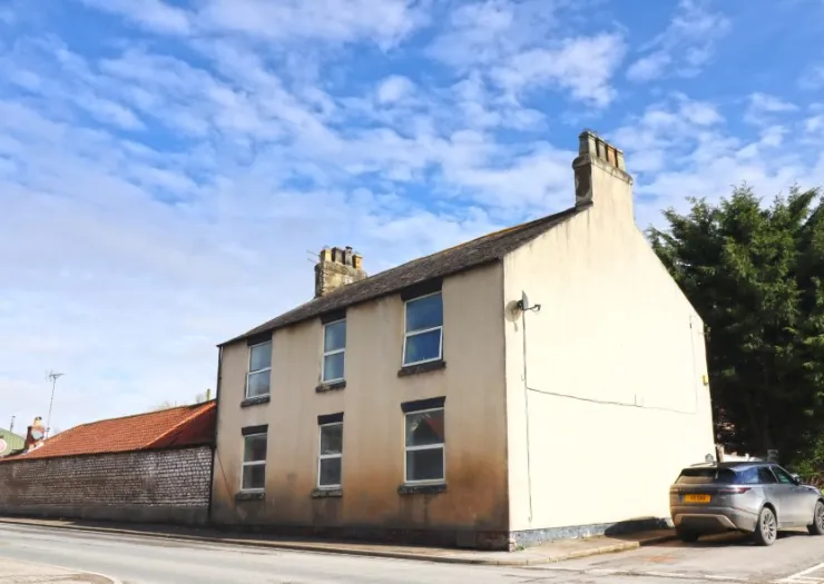 Cream-colored two-story house with multiple windows and chimneys, viewed from the street corner.