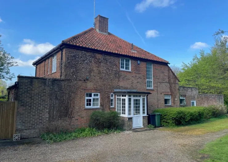 Red brick house with white porch and climbing ivy, under a blue sky.