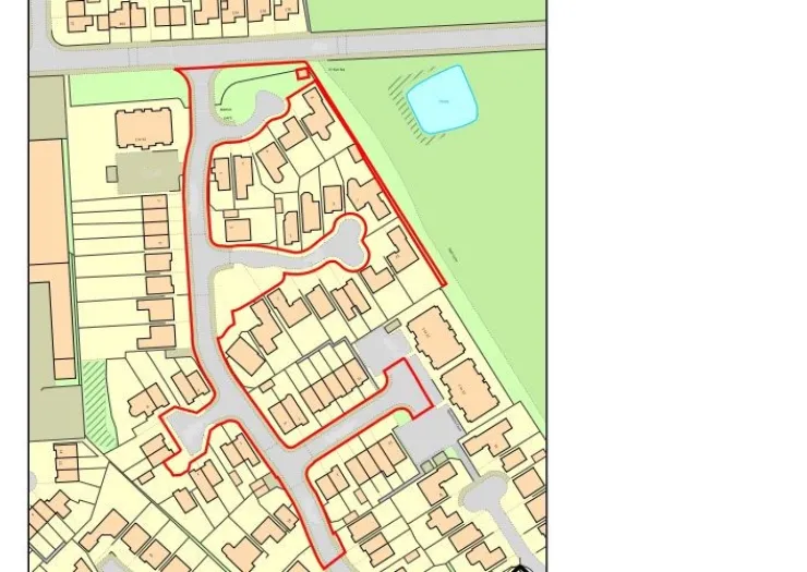 Site plan highlighting a housing development with a red border, adjacent to a road and small pond.