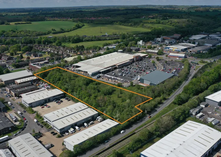 Aerial view of commercial land for sale, outlined in orange, surrounded by industrial units and retail parks.