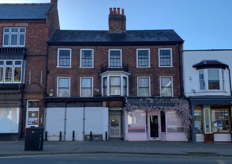 Brick building with white-trimmed windows and a bay window, situated between other commercial properties.