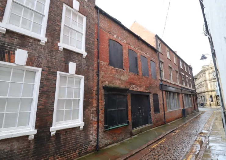 Brick buildings with boarded-up windows and doors on a cobblestone street.
