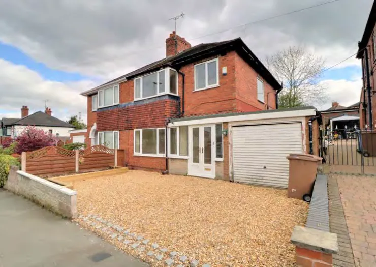 Red brick house with attached garage, gravel driveway, and wooden fence.