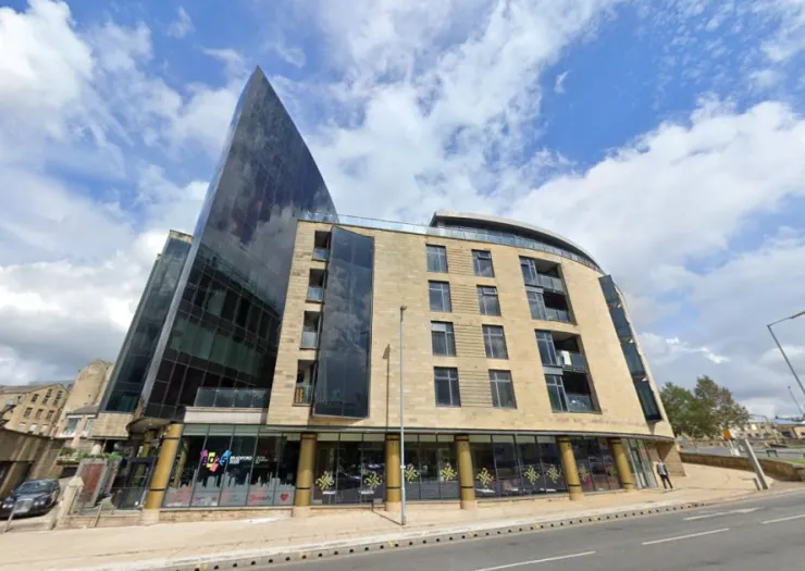 Modern mixed-use building with angled glass facade and sandstone exterior under a blue sky.