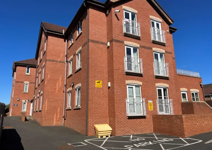 Modern red brick apartment building with white balconies under a clear blue sky.