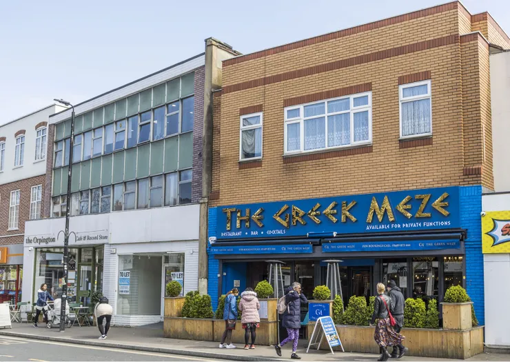 The Greek Meze" restaurant exterior with people outside, plus adjacent shops to let.