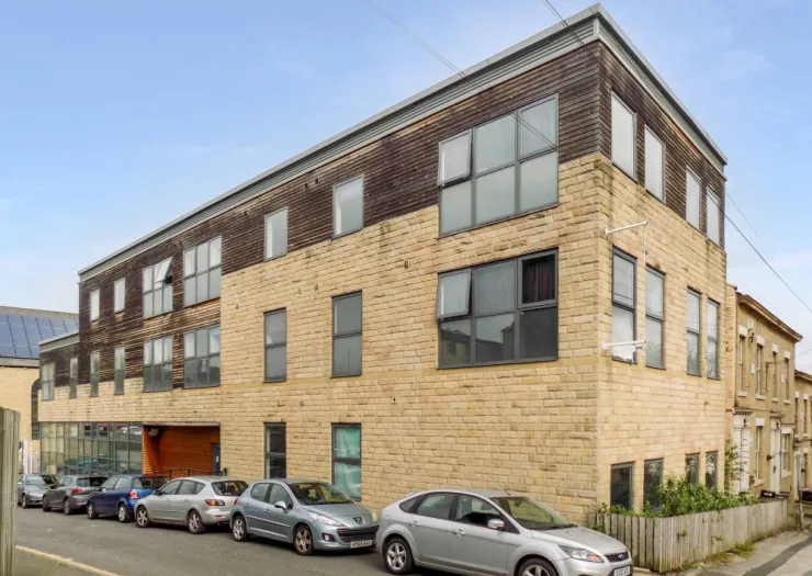 Modern apartment building with wood and stone exterior, multiple windows, and parked cars on street.