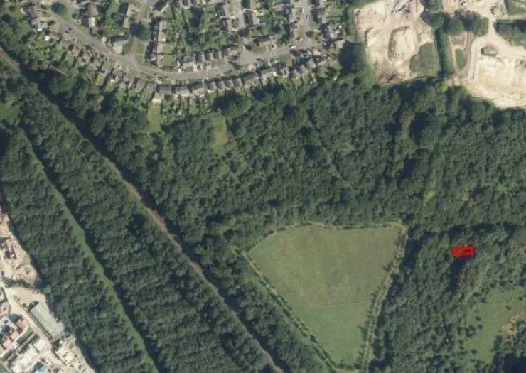 Aerial view of green field, trees, housing, and a quarry.