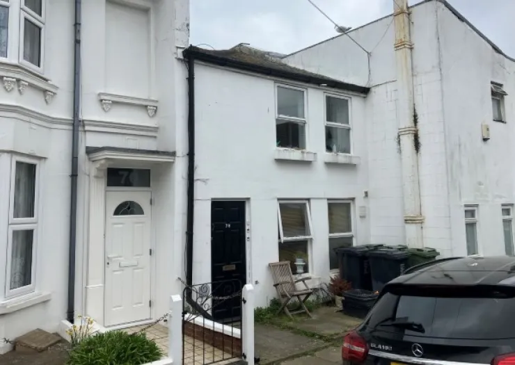 White terraced house exterior with black front door, visible house number and bins.