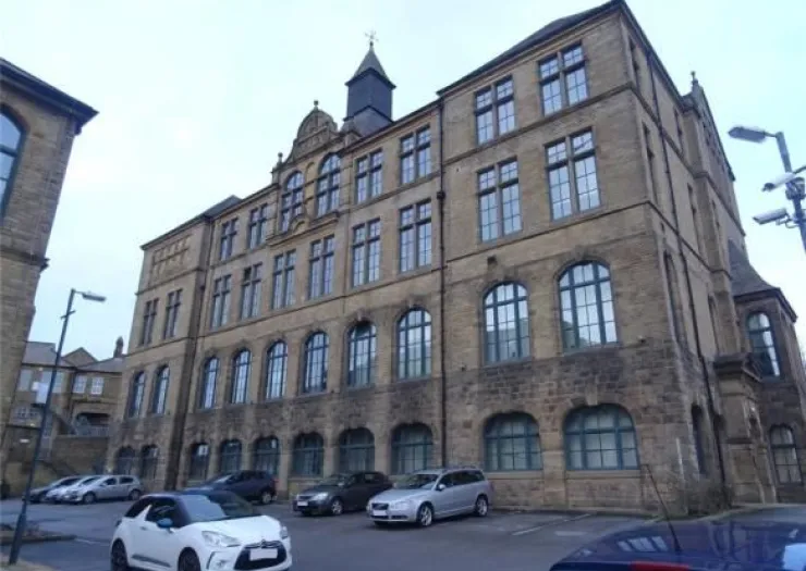 Grand stone building with arched and rectangular windows, a small spire, and cars parked in front.