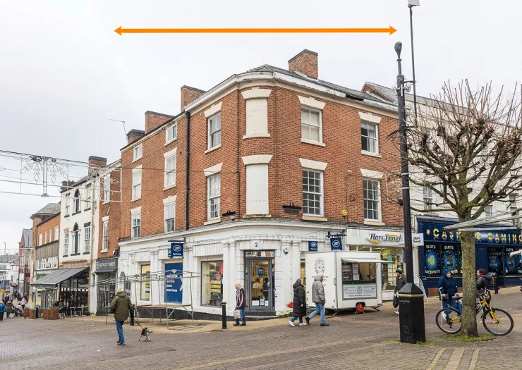 Red brick building on a UK high street with Boots and Hays Travel signage. Pedestrians and a small kiosk are visible.