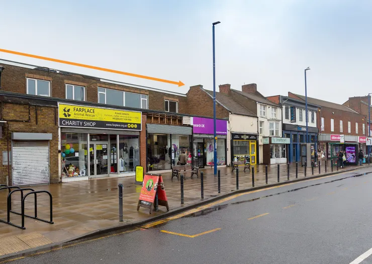 Row of commercial units on a UK high street, some occupied, on an overcast day.