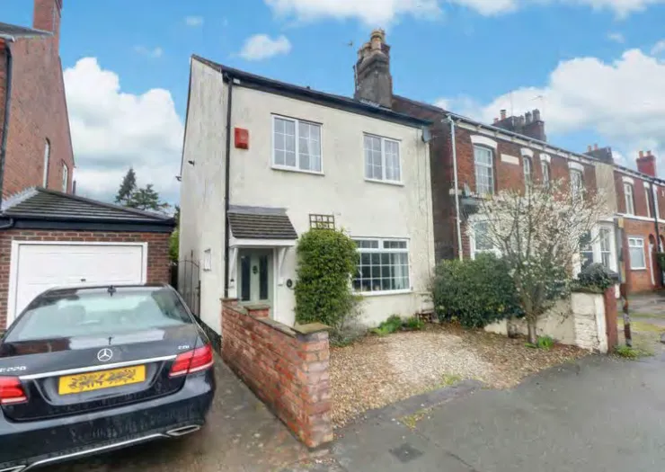 White two-story house with green front door, gravel driveway, and attached garage.