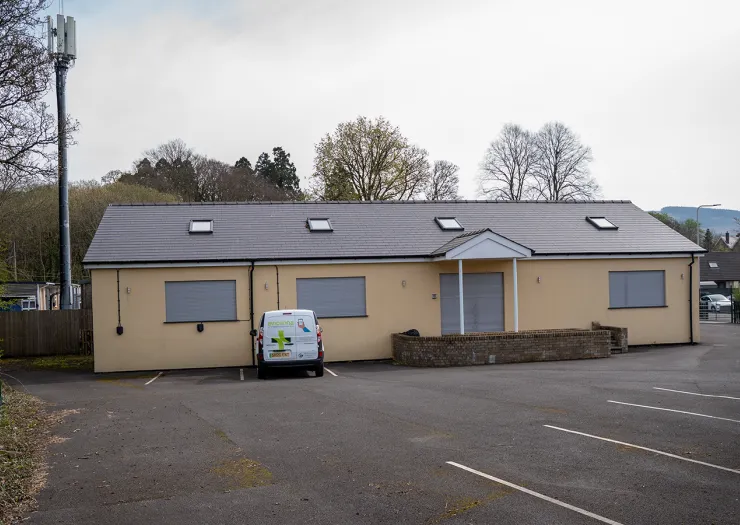 Beige single-story building with dark gray roof, skylights, and a "MedicNow" van parked in front.