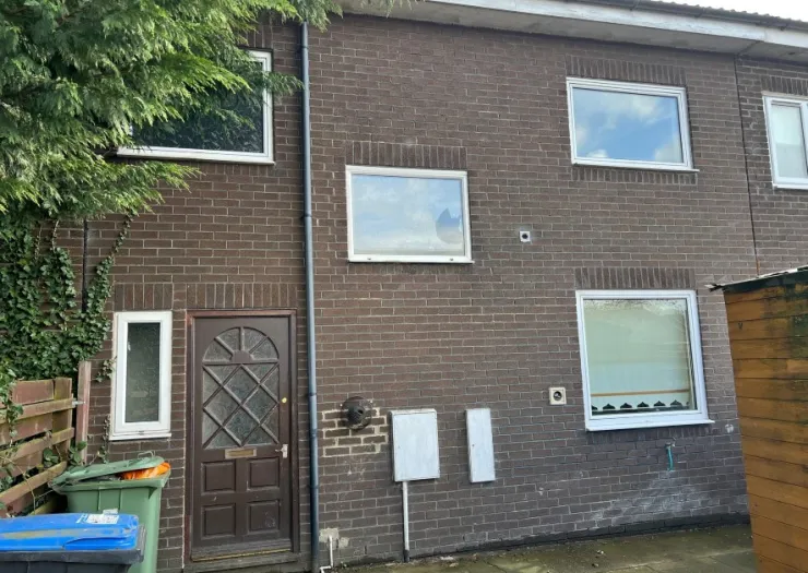 Brown brick terraced house exterior with white-framed windows and dark wood front door.