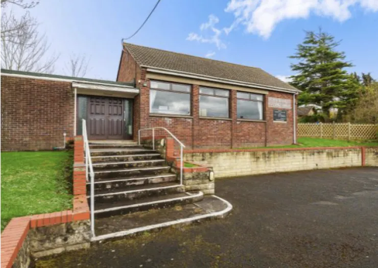 Red brick building with steps and railings leading to a double door entrance.