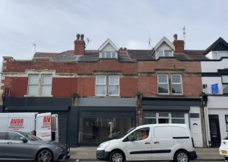 Red brick commercial property with vacant storefront and upstairs apartments.