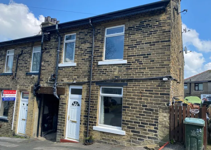 Stone terraced house with white front door and windows, under a blue sky. "Sold at Auction" sign visible.