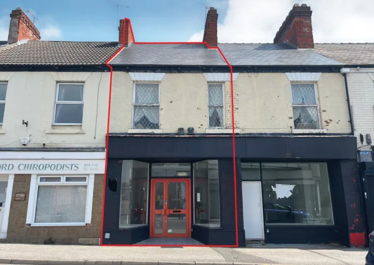 Retail property with black storefront and orange double doors, two upper-level windows, and slate roof.