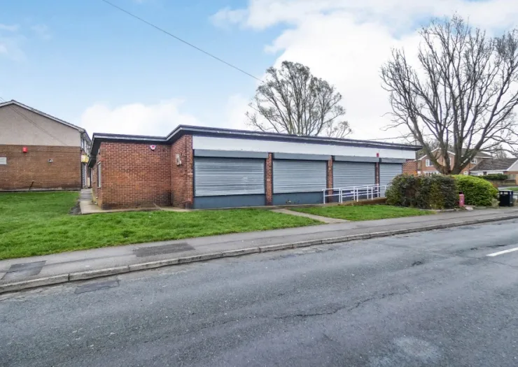 Brick retail building with metal security shutters, ramp access, and roadside parking.