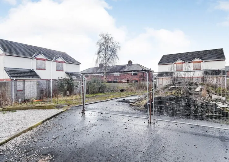 Boarded-up houses, demolition rubble, and metal fencing on a residential street.