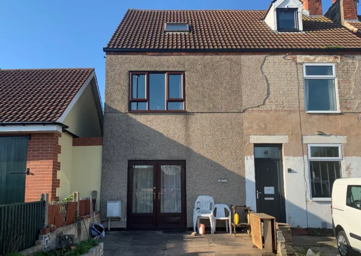 Two-story terraced house exterior with brown roof, pebbledash and brick walls, and brown doors and windows. Some exterior rep