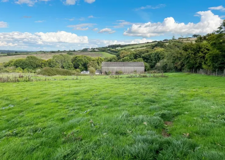 Green field with a barn, trees, and rolling hills under a blue sky with fluffy white clouds.