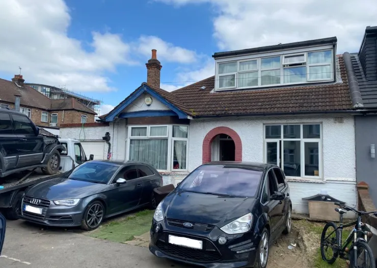 White suburban house with dormer loft conversion and cars parked in front.