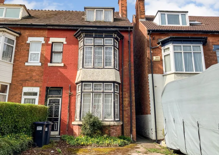 Red brick terraced house with bay windows and lace curtains. Needs renovation.