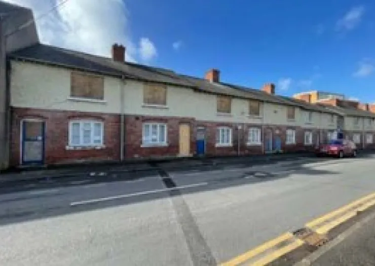 Row of brick terraced houses with boarded-up windows.