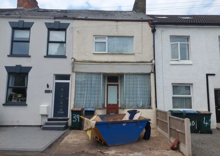 Terraced house exterior with large blue skip in front garden. Renovation project.