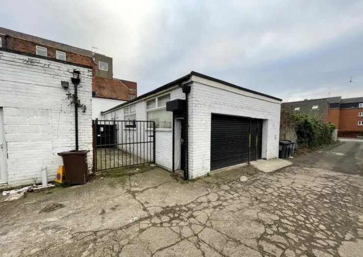 White brick industrial unit with black roller door and gated yard.