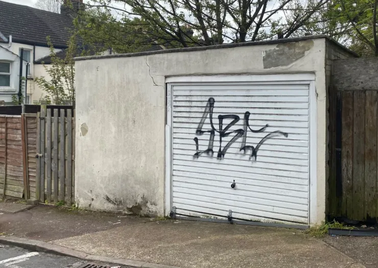 White garage door with black graffiti, cracked concrete wall, and wooden fence.