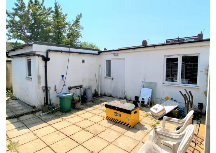 White outbuilding with patio, gardening tools, and storage box. Needs renovation.