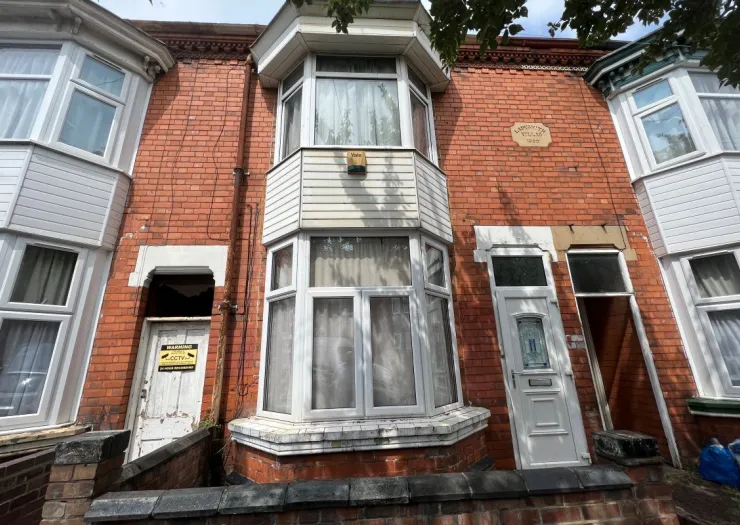 Red brick terraced house with bay window, "Lambourne Villas 1900" plaque, and CCTV warning sign.